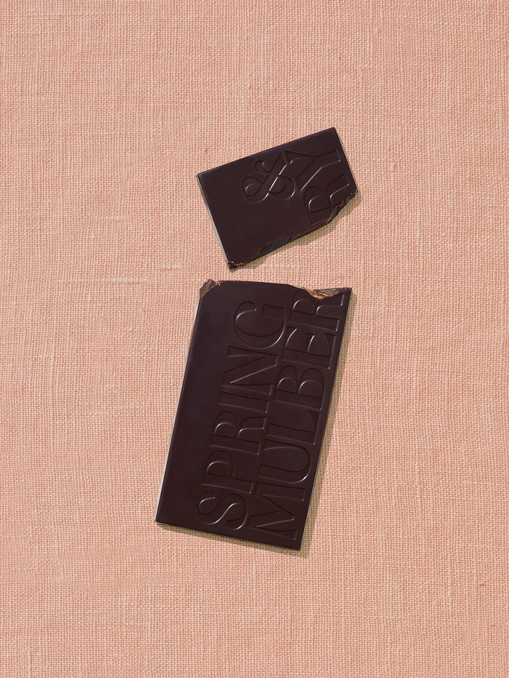 Dark chocolate bar with a piece missing on a pink textured background