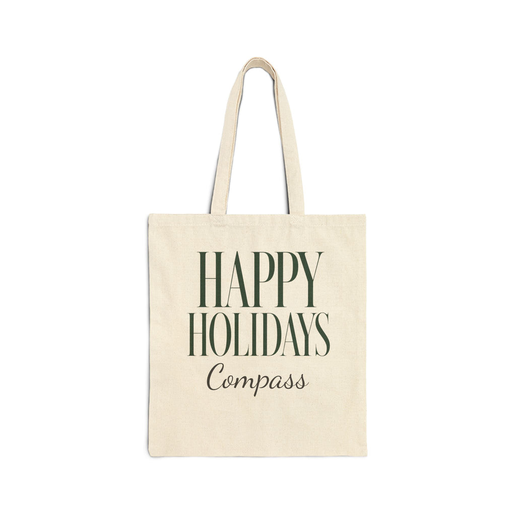 An off-white canvas tote bag with dark green text reading 'HAPPY HOLIDAYS Compass' on the front, shown against a plain white background.