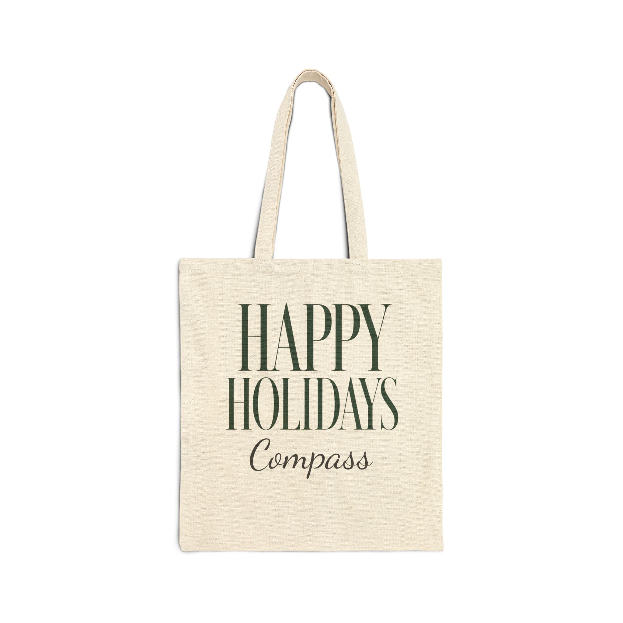 An off-white canvas tote bag with dark green text reading 'HAPPY HOLIDAYS Compass' on the front, shown against a plain white background.