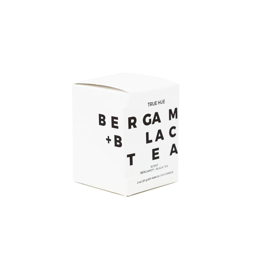 True Hue bergamot and black tea mini candle with a sleek glass container and lit wick, creating a cozy ambiance.