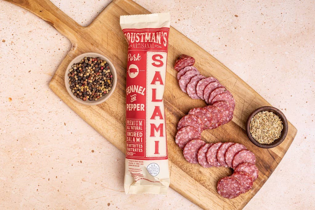 Goustman's Salami packaging on a wooden board with sliced salami and pepper mix.