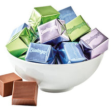 Bissinger's chocolate bars in colorful wrappers in a white bowl with additional chocolate bars on a white background.