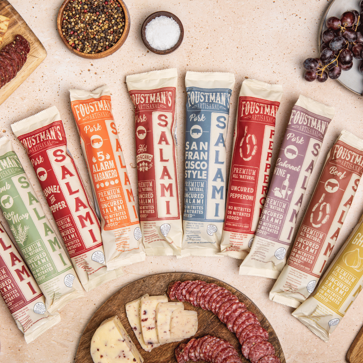 Assorted Foustman's Salami packages on a table with salami slices and cheese.
