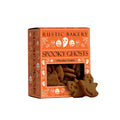 A box of Rustic Bakery Spooky Ghosts chocolate cookies on a light beige surface with a matching background. The orange packaging features white Halloween-themed illustrations, and several ghost-shaped cookies are displayed in front of the window.