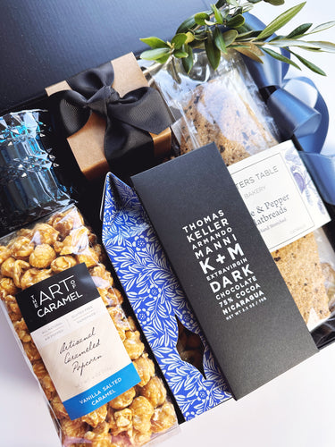 Gift basket with chocolate, popcorn, and a bottle of wine on a white surface.