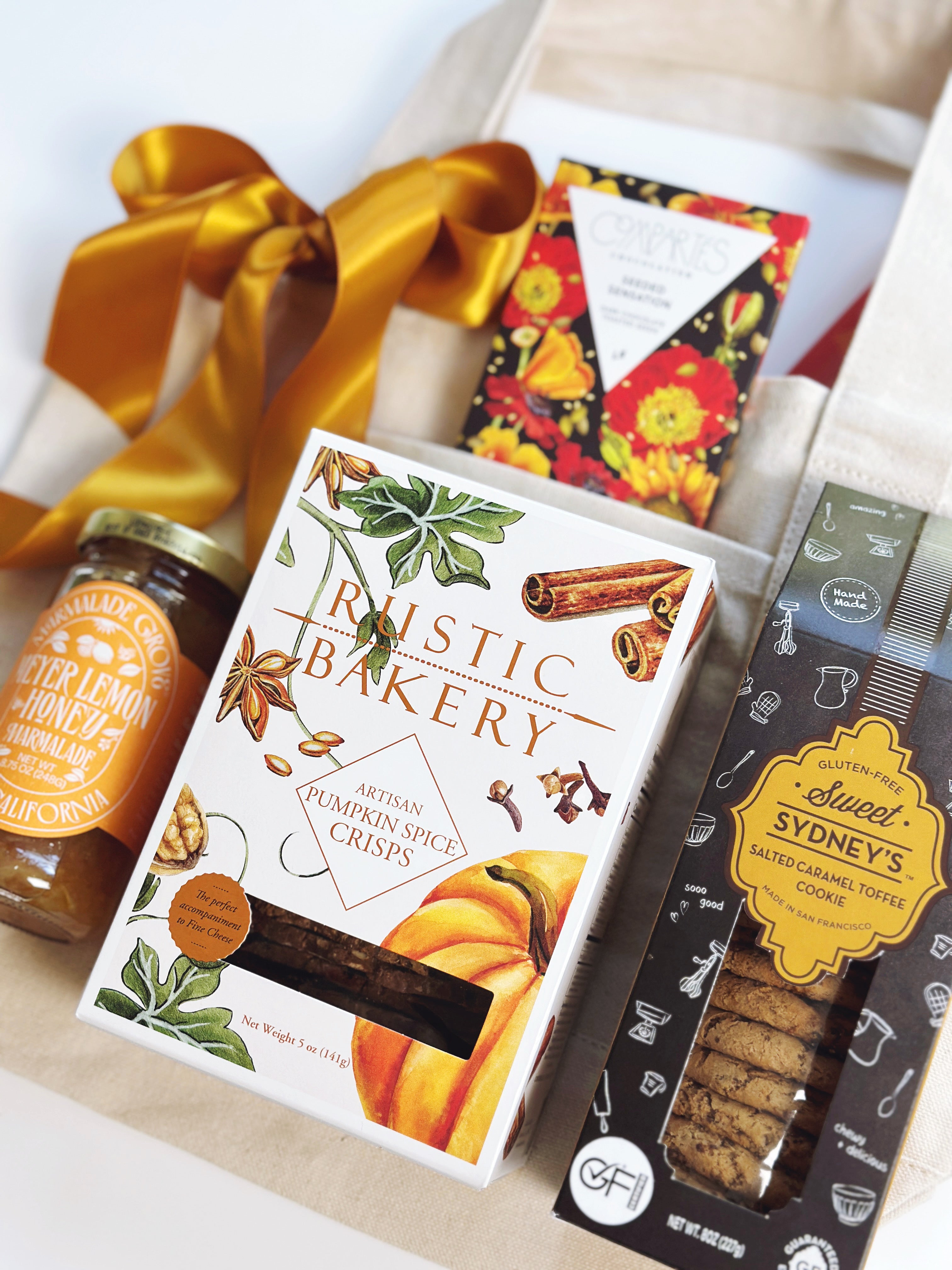 A tote bag with jam, rustic bakery pumpkin spice crisps, Salted Caramel cookies and chocolate bar lying on top.