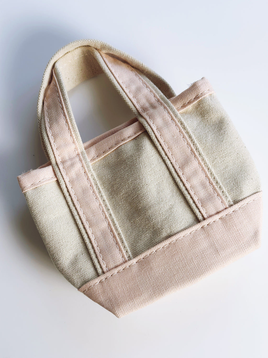 A small canvas tote bag in a light beige fabric with contrasting dusty pink trim and handles, shown on a plain white background.