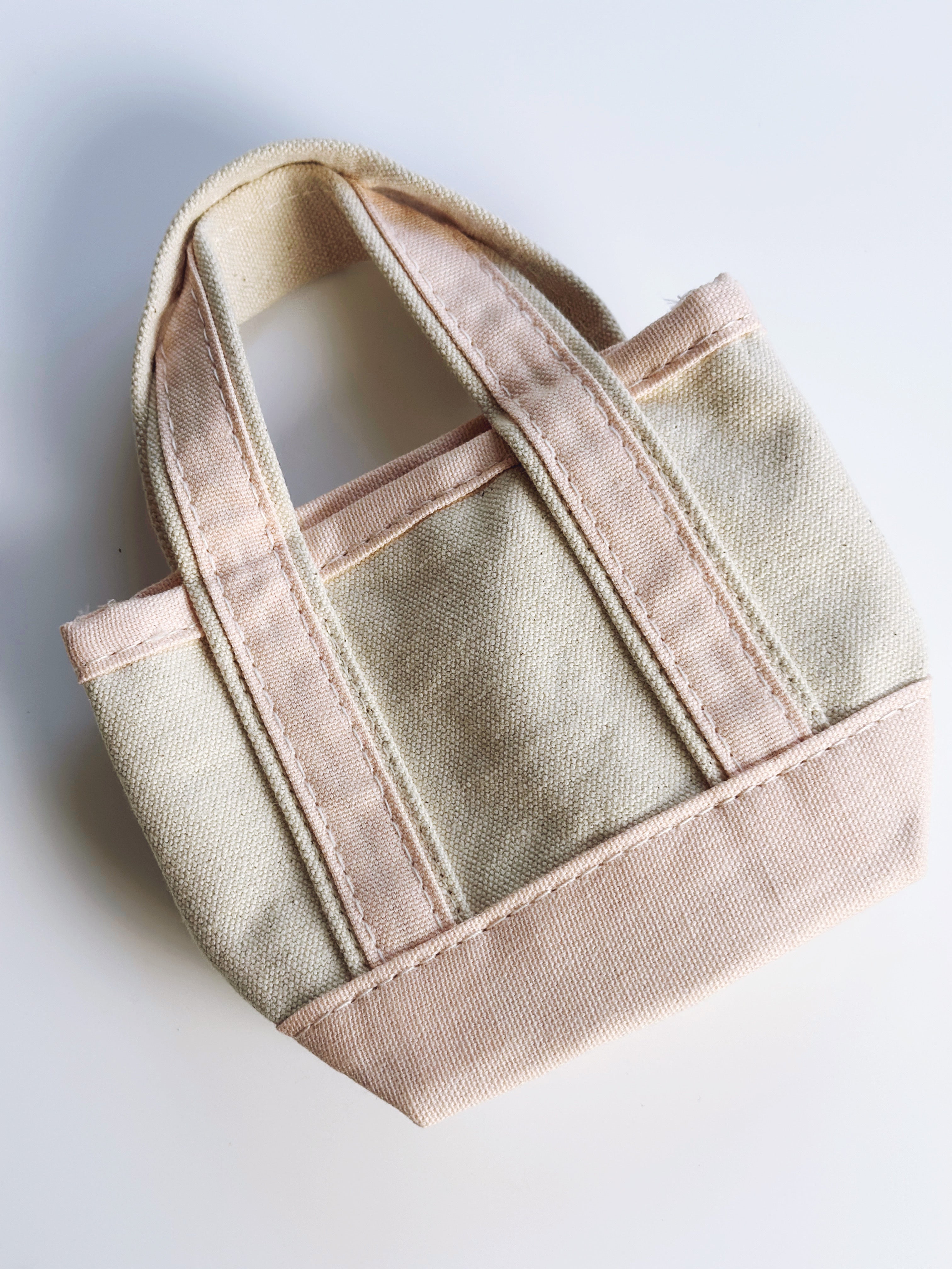 A small canvas tote bag in a light beige fabric with contrasting dusty pink trim and handles, shown on a plain white background.