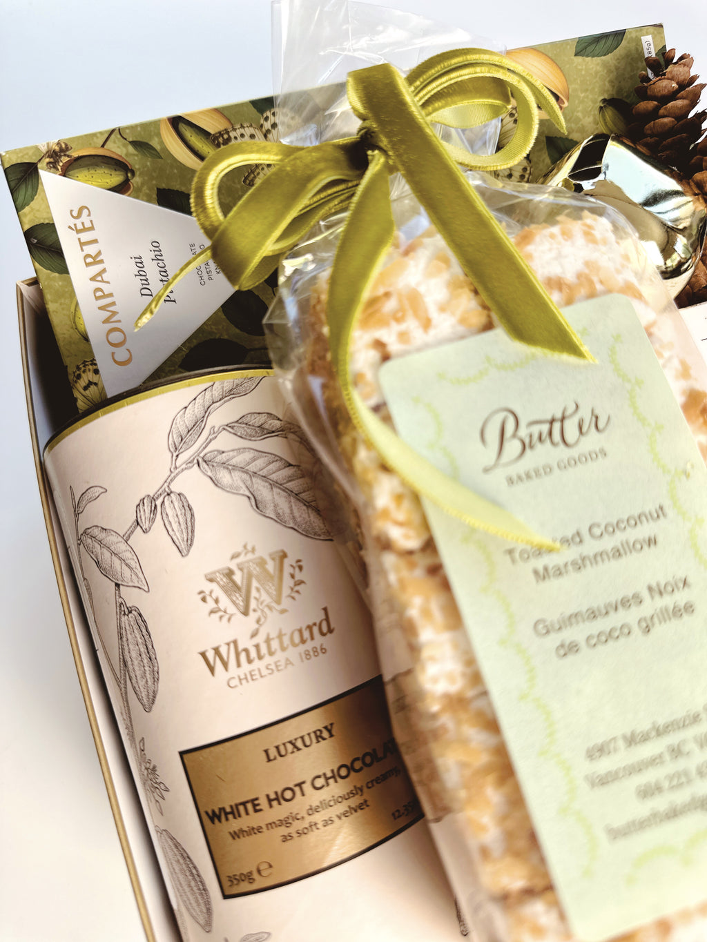 A gourmet gift box with Whittard Chelsea 1958 featuring a can of White Hot Chocolate and a packaged bag of Toasted Coconut Marshmallow, tied with a green velvet ribbon.