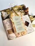 A gourmet gift basket with Whittard white chocolate cocoa and Rustic Bakery gingerbread, featuring a bag of toasted coconut marshmallows tied with a green velvet ribbon.  Tucked at the top is a Dubai Pistachio Chocolate Bar.