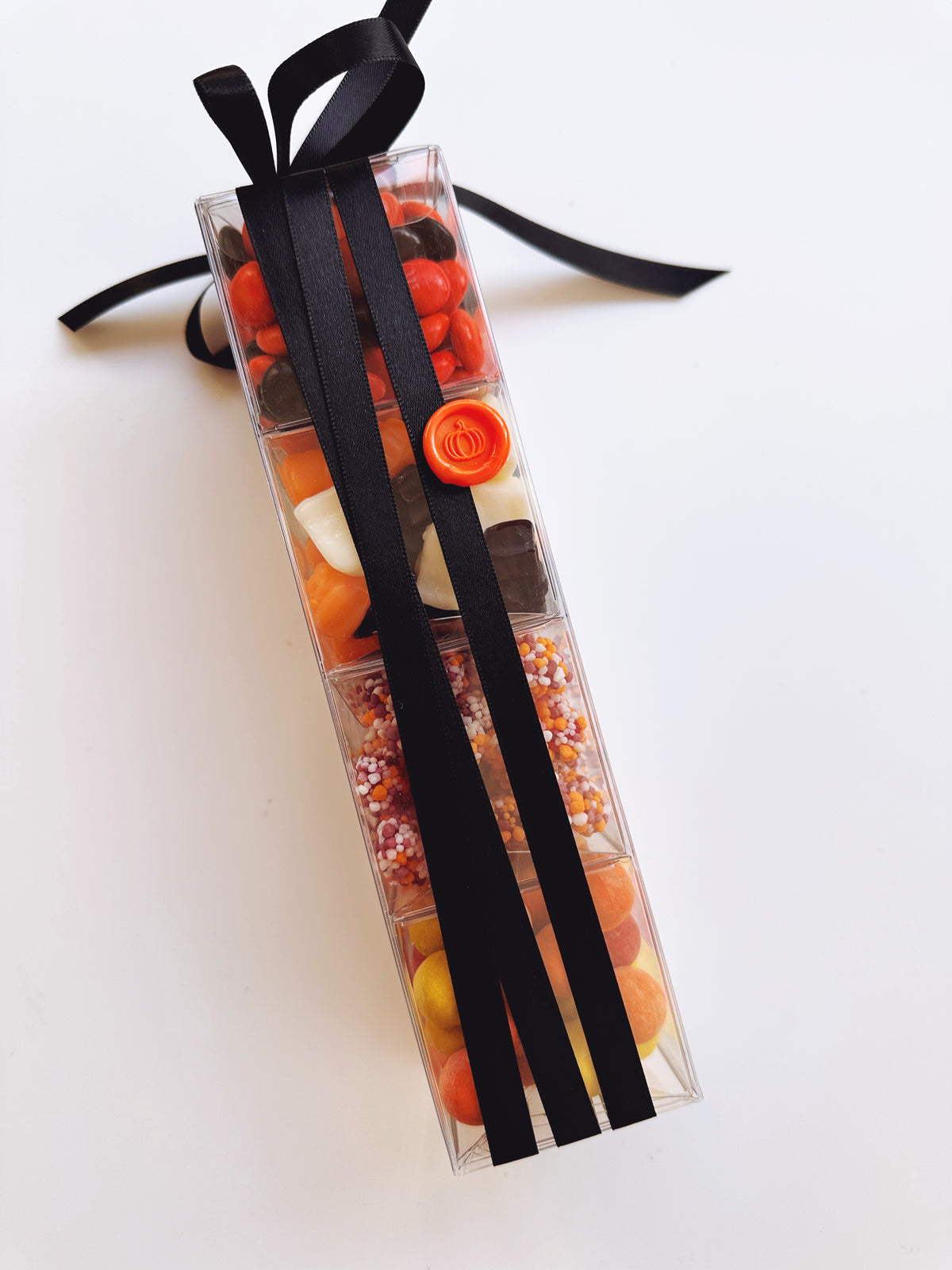 A clear plastic gift box filled with assorted halloween candies and chocolates, tied with a black ribbon, photographed on a plain white background.