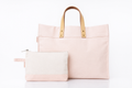 A light pink canvas tote bag with tan leather handles, shown with a matching small zip pouch in front on a white background.