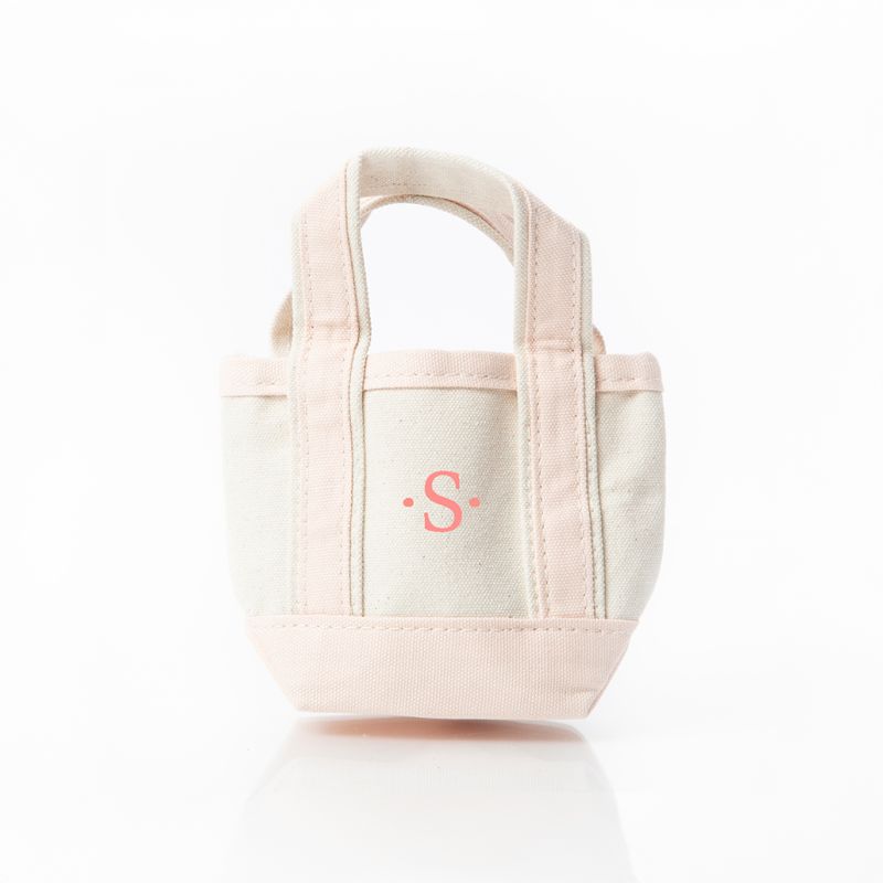 A small canvas tote bag in a soft cream and pale blush pink colorway, featuring a pink embroidered monogram 'S' on the front, set against a clean white background.