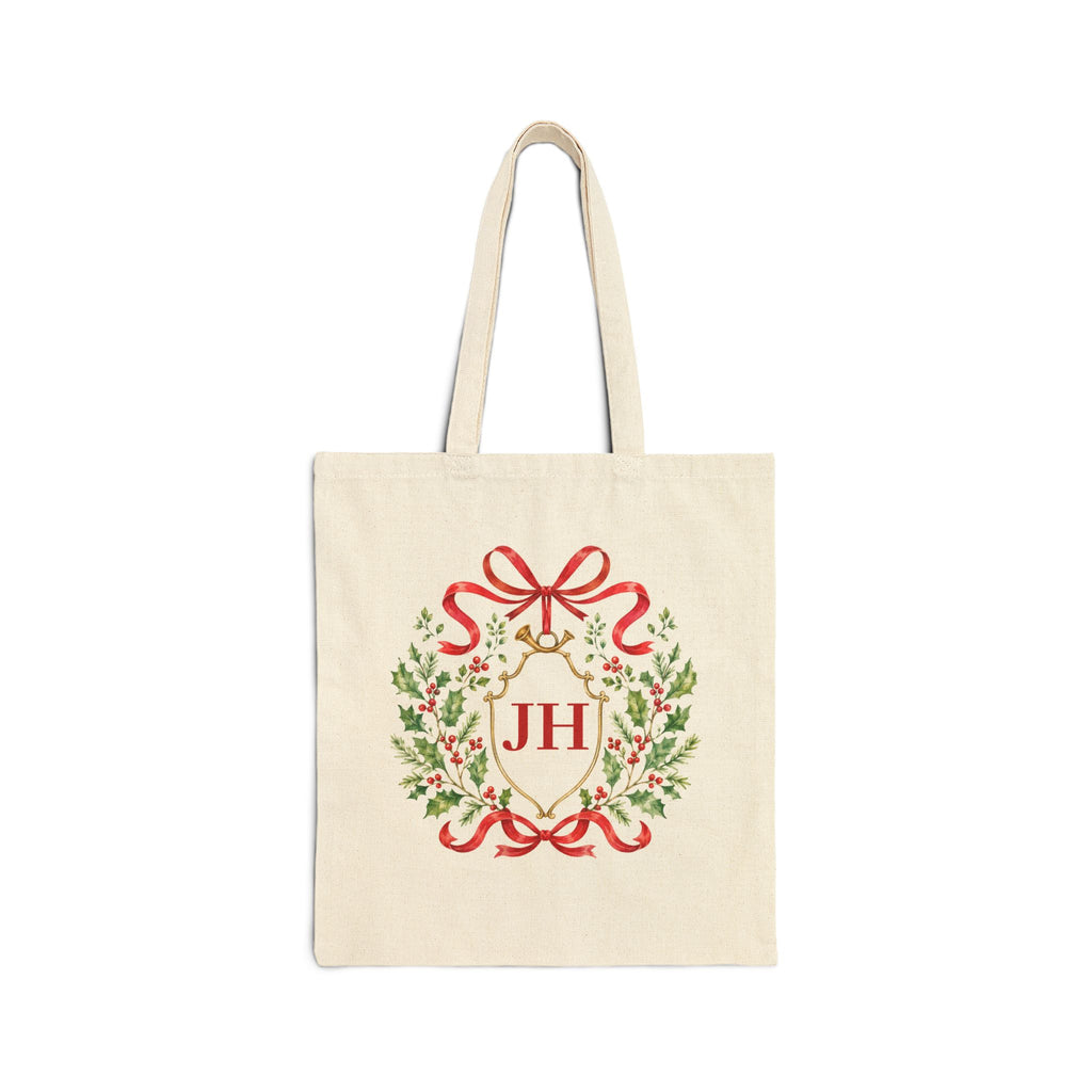An off-white canvas tote bag with a Christmas wreath design featuring green holly leaves, red ribbons, and a gold monogram 'JH' on the front, set against a plain white background.