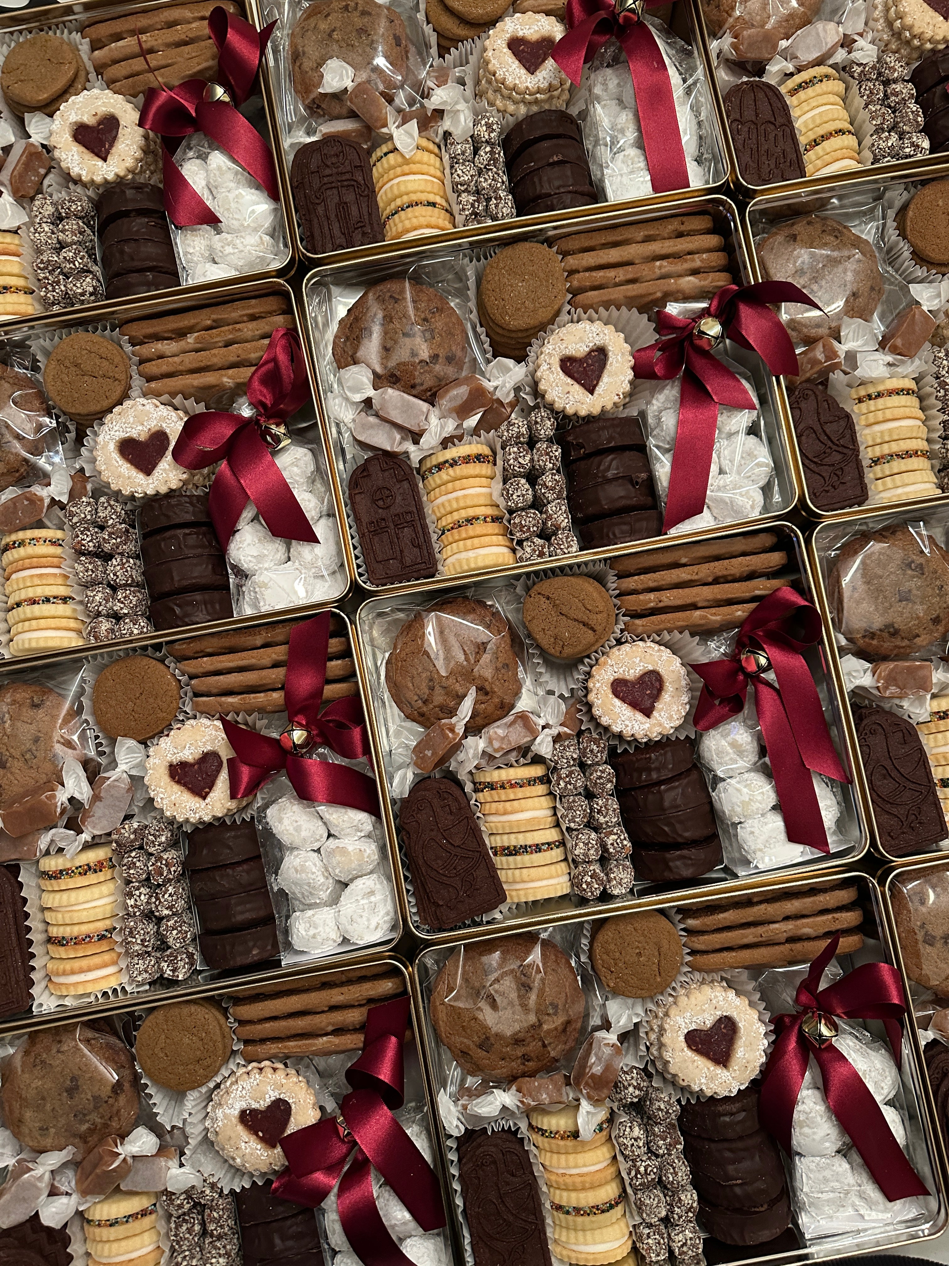 Rows of holiday tins filled with assorted Christmas cookies.
