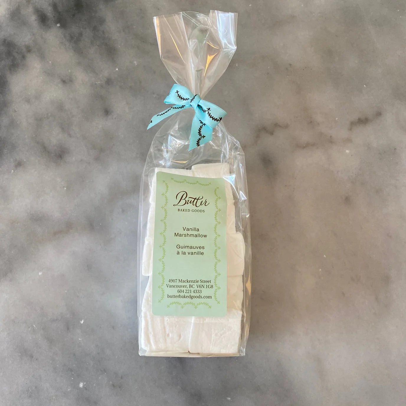 A clear plastic bag containing several white marshmallows, tied with a light blue ribbon, and labeled 'Butter' on a marble-like gray background.m