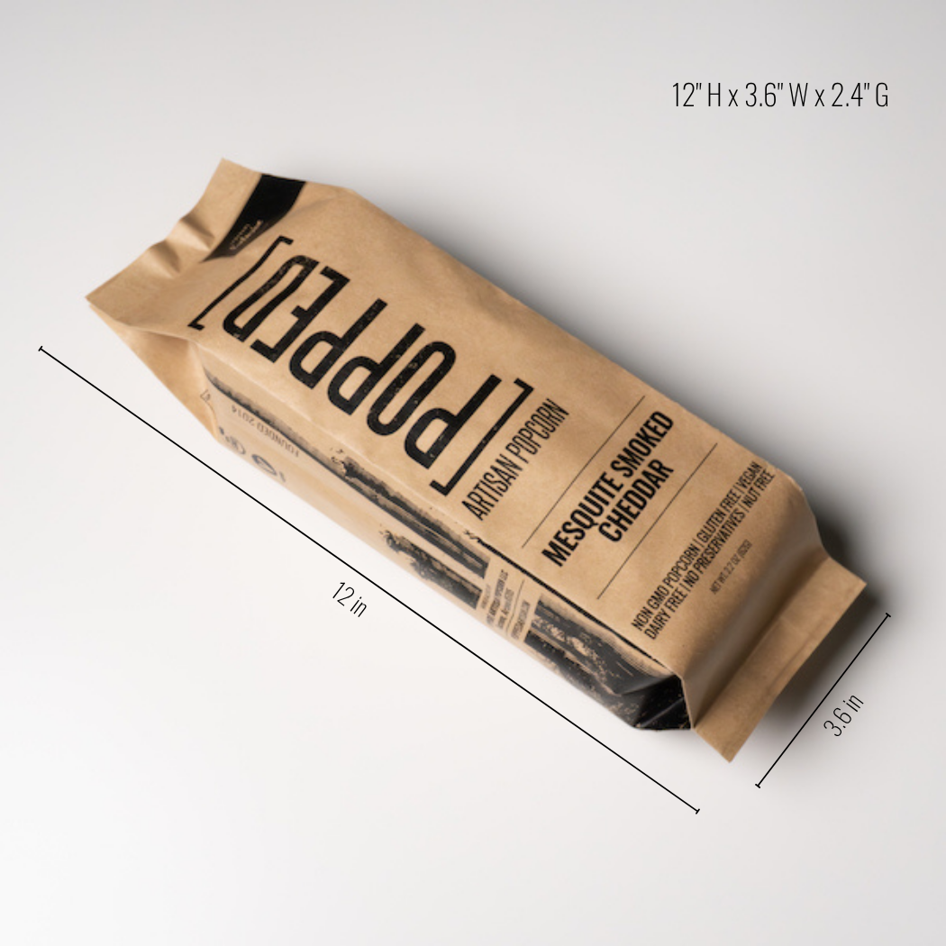 A kraft paper bag of Popped Artisan Popcorn, Messuty Smoked Cheddar, shown on a light gray background with black dimension lines and text indicating its size as 12" H x 3.6" W x 2.