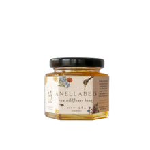 Jar of raw wildflower honey from Anellabees, a natural condiment, with a golden honeycomb and fresh wildflowers in the background.