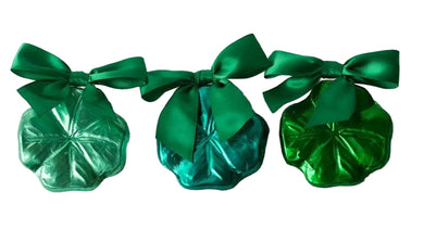 Three green metallic candy packages with bows on a light gray background