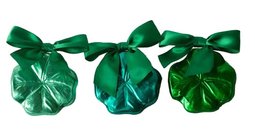 Three green metallic candy packages with bows on a light gray background