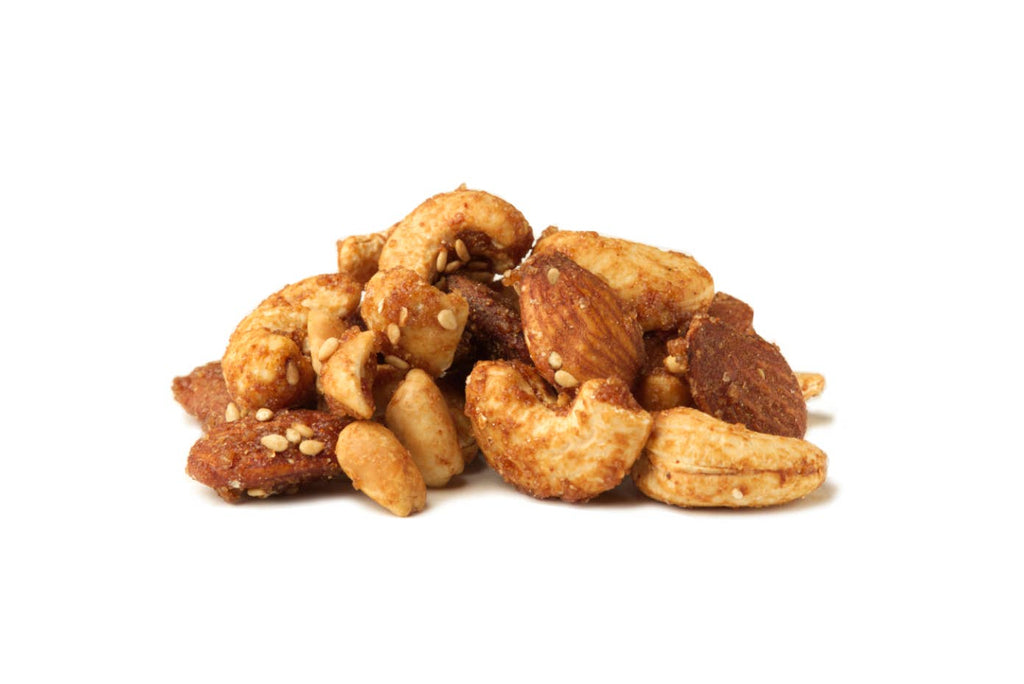 A small pile of mixed nuts, including cashews, almonds, and dried fruit pieces, lightly coated with seasoning and topped with sesame seeds, isolated on a white background.