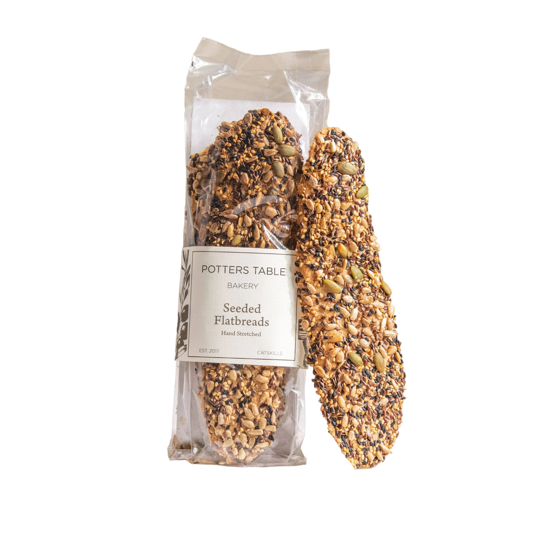 Packaged seeded flatbreads from Potters Table with a Good Food Award badge on a neutral background