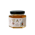 Glass jar of raw wildflower honey from Anellabees, showcasing golden honey with wildflower blossoms in the background.